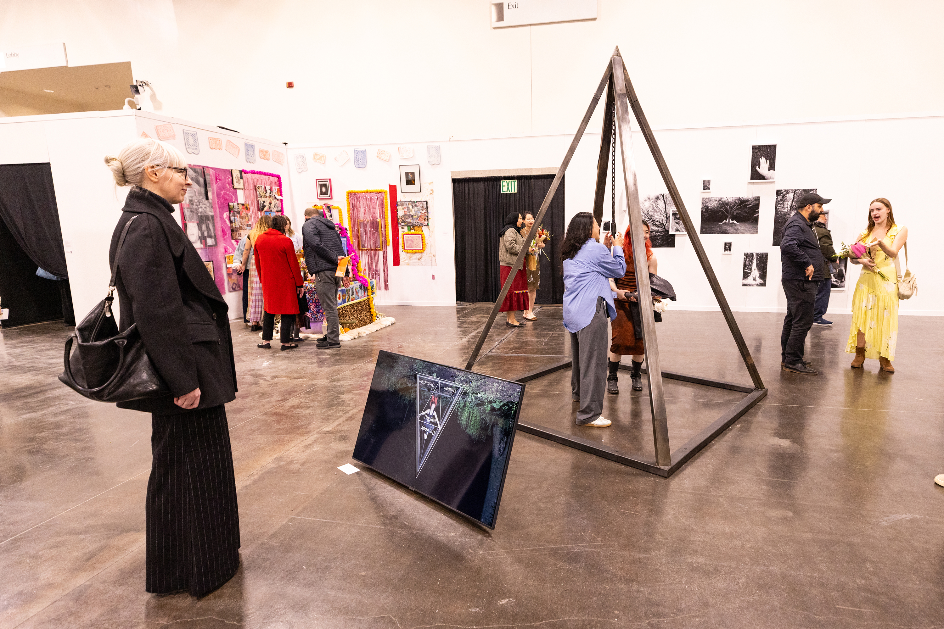 viewer at Grad Show studies a large metal pyramid-shaped sculpture