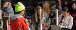 alumna in orange jacket stands behind a table at RISD CRAFT as shoppers look at the jewelry on display