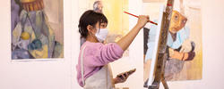 Student painting in studio with paintings on the wall.