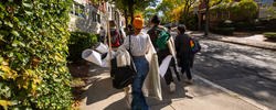 a group of students holding their work are walking up the hill alongside the freshman quad on a sunny day