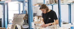 architecture student works on a model in a room surrounded by art materials