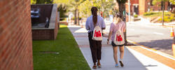 two students wearing backpacks that say "hi" on them walk down the hill along the freshman quad