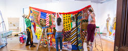 three students installing a large textiles project with colorful pieces of fabric draped over one another