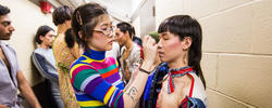 a student applies makeup to a model in a backstage area