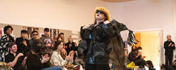 model in an extravagant black outfit walks down a runway surrounded by an audience
