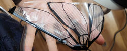 a hand holds a translucent synthetic object shaped like a butterfly