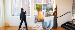 Students hanging a large painted piece of fabric in a brightly lit studio