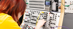 a student turns a small knob on a large analog synthesizer