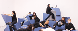 several students sit or lounge atop light blue, angular furniture inside an all-white room
