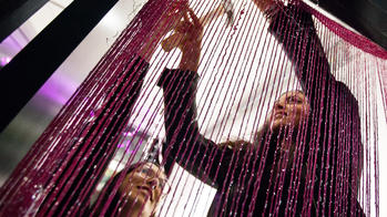 a RISD student uses a hammer to hang long, lit magenta threads from a doorway