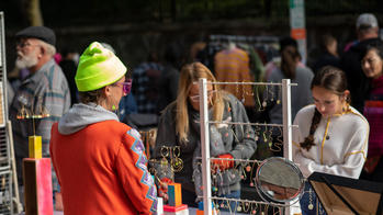 alumna in orange jacket stands behind a table at RISD CRAFT as shoppers look at the jewelry on display