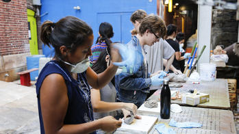 students at outdoor workstations shape clay into sculptures