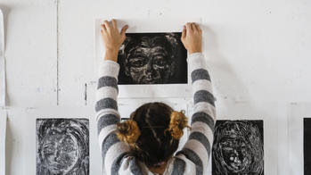 a student pins a black and white illustration above other works of art on a wall