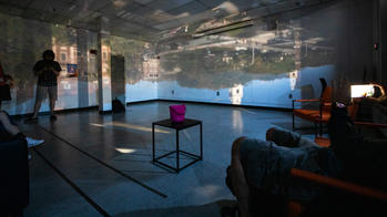 a video installation fills a dimly lit gallery space as visitors observe