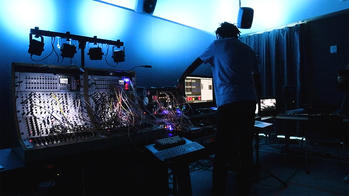 student working on a synthesizer in a darkened sound studio