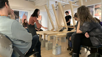 a R I S D student displays a wooden structure to faculty and other students inside a studio classroom