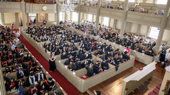grad students in robes and regalia fill the pews of the First Baptist Church in America