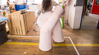 a student shapes a pinkish-white abstract sculpture in a large, industrial studio space