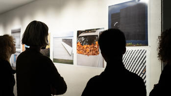 Students and faculty observe a series of photographs mounted on a wall