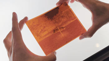 two hands hold a rust-colored photo of an outdoor space against a light table