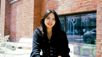 Alicia Lee in a black long sleeved top standing in front of a brick and glass building