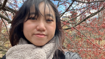 Elizabeth Tjahja in a black jacket and fuzzy light brown scarf in front of a blooming tree