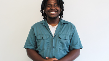 Nahom Ghebredngl in a shortsleeved blue button down shirt smiling against a grey background