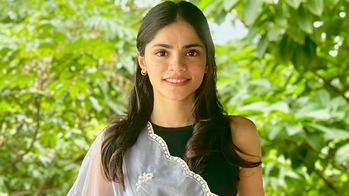 Raveena Deshpande in a black sleeveless top with a gauzy cloth draped over her shoulder in front of a green leafy background