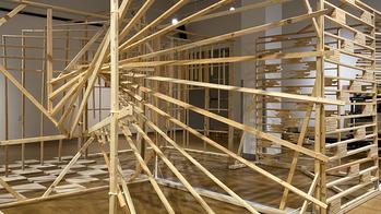 a large wooden structure with several wooden "spokes" bursting from a vertical beam sits inside a studio space
