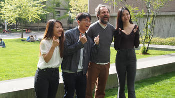three students stand alongside R I S D faculty member Paolo Cardini on the green lawn of a college campus
