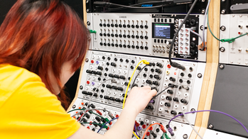 a student turns a small knob on a large analog synthesizer