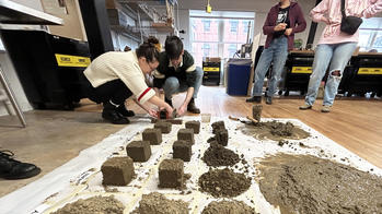 students stand around clay samples arranged on a workshop floor, with labels classifying the clay types as "compacted", "tamped" and "filled"