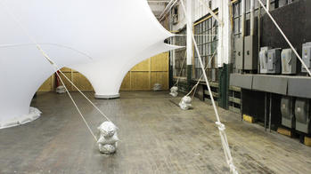 a large, tent-like white structure stretches from floor to ceiling, tied to props on a studio floor