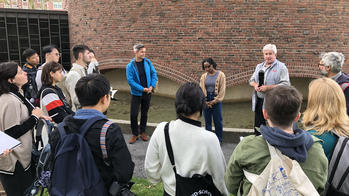 several people gathered outdoors in a courtyard with a large brick exterior in the background