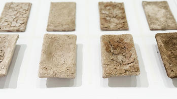 a three row, four column grid of rectangular, off-white clay pieces elevated on a white surface