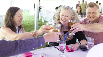 A group of people are toasting together at a table during RISD's reunion weekend.