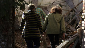 two people hold hands as they walk outdoors through rubble