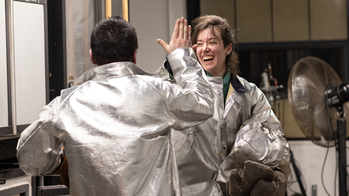Two students in protective gear in the hot shop high five-ing  