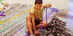 artist Bhen Mark sits on the floor weaving plastic strips