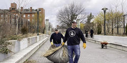 Two Alumni volunteers carrying leaves at a cleanup event
