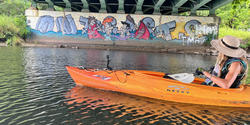 Associate Professor Emily Vogler kayaks under a bridge along the Blackstone River