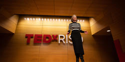 Amy Devers, host of the event, stands on stage in the Chase Auditorium with the TEDxRISD sign behind her