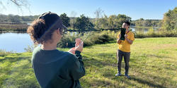 two students hold mirrors to reflect the sun next to the Blackstone River