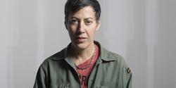 Photography of painter Nicole Eisenman wearing a red t shirt and green jacket.