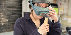 a student wearing an opera visor closely inspects a platinum ring she is working on
