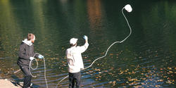 faculty member Max Pratt throws a sample-collecting bucket into the Blackstone River