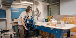 student uses a hand-powered wheel to flatten a slab of clay
