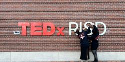 Two people hand up TEDxRISD lettering