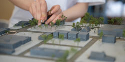 a student glues miniature trees to a large 3D model of a site in Detroit