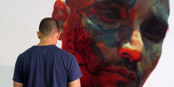 the artist at work on a huge painting of a man's tattooed face